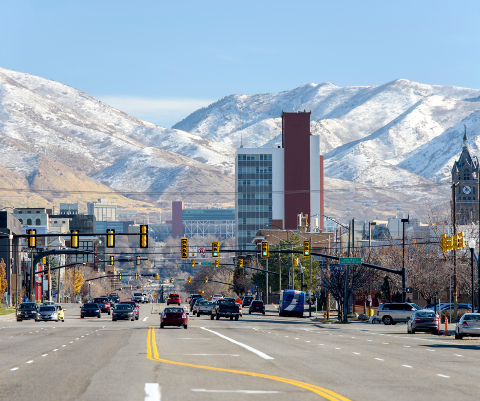 A city street with a tall building and snowy mountains in the background.