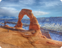 A large rock on a beach with Arches National Park in the background.