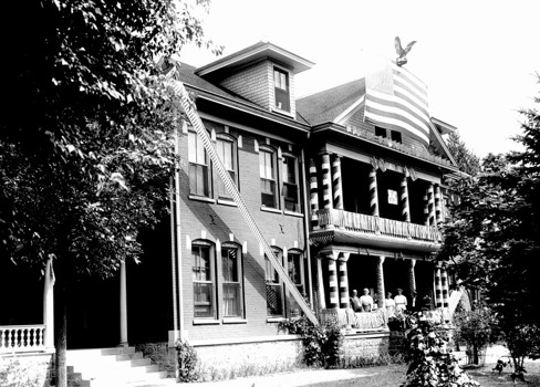 A large house with a few people sitting on the porch.