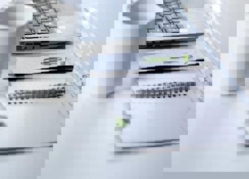 A stack of papers next to a laptop.