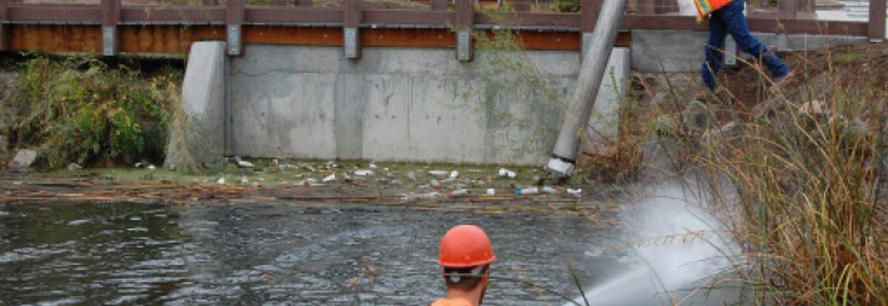 A man on a ladder in a river with a man on a bicycle.