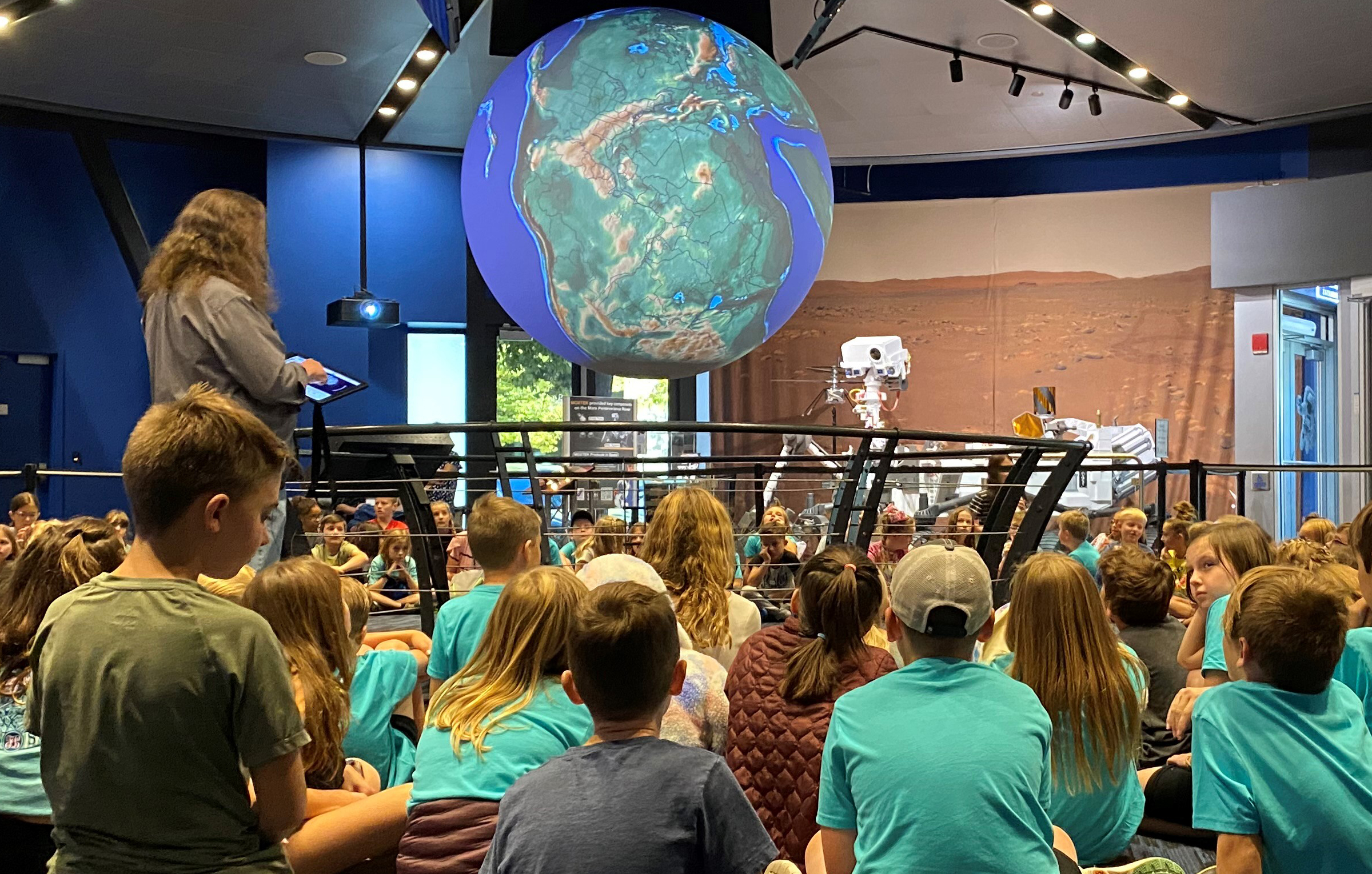 A person speaking to a group of people in a room with a large globe.