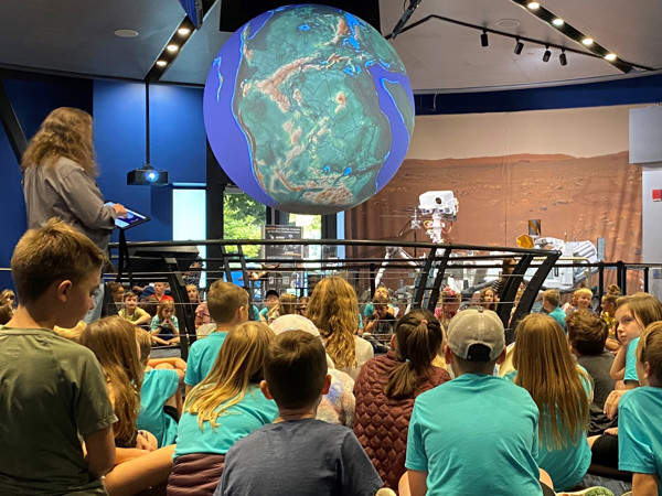 A person speaking to a group of people in a room with a large globe.
