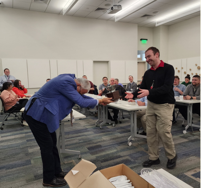 A person handing another man something on the laptop.