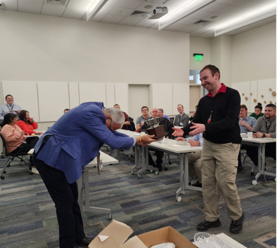 A person handing another man something on the laptop.