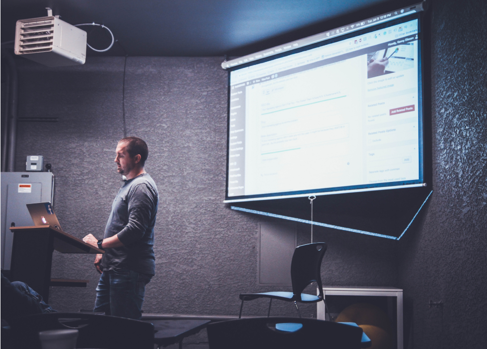 A man standing in front of a projector screen.