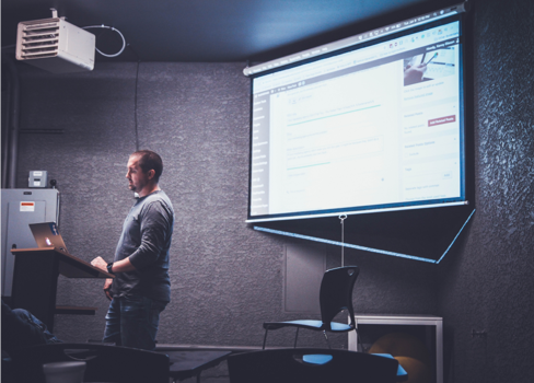 A man standing in front of a projector screen.