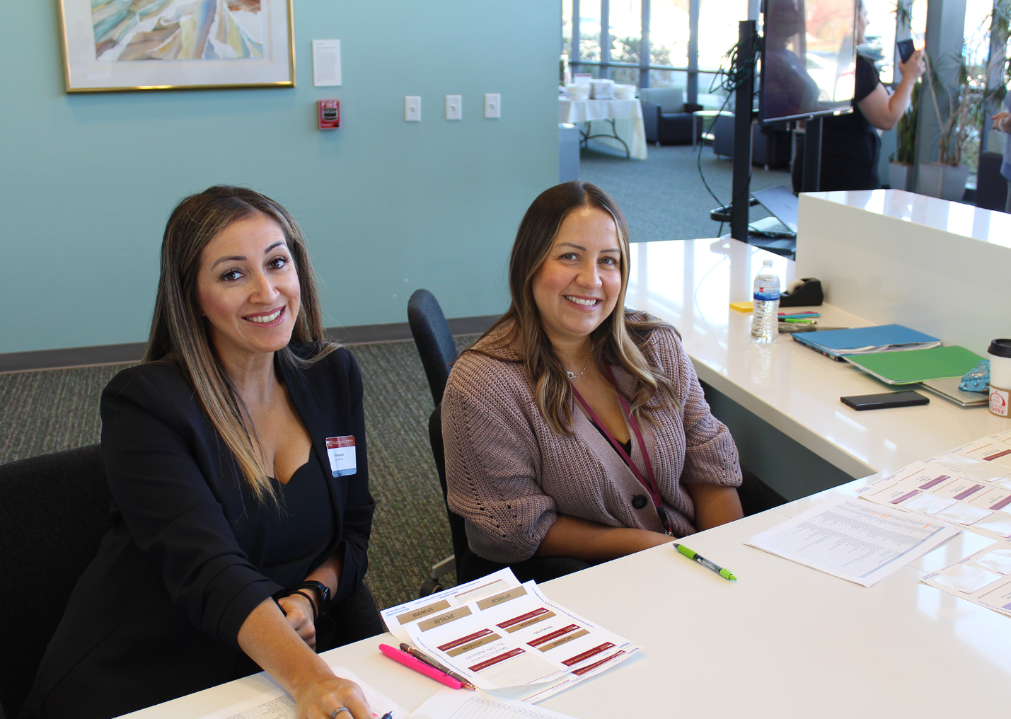 A couple of women sitting at a table with papers and pens.