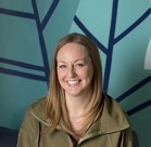 A person smiling in front of a blue wall.