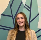 A person smiling in front of a wall with a blue and yellow background.