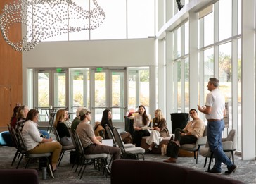 A person talking to a group of people sitting in chairs.