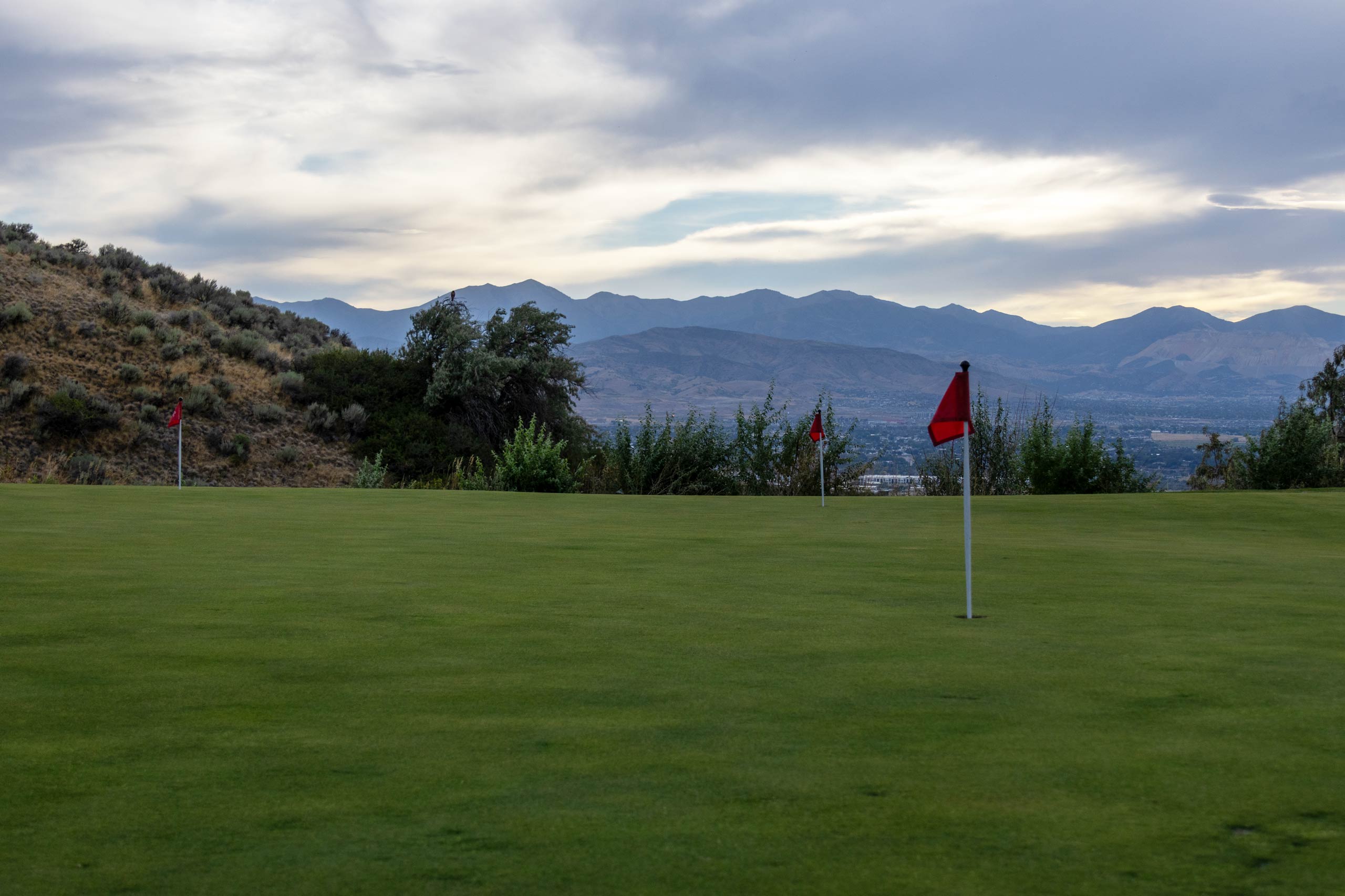 A putting green with flags at South Mountain golf course in Salt Lake City, with trees and mountains in the distance.