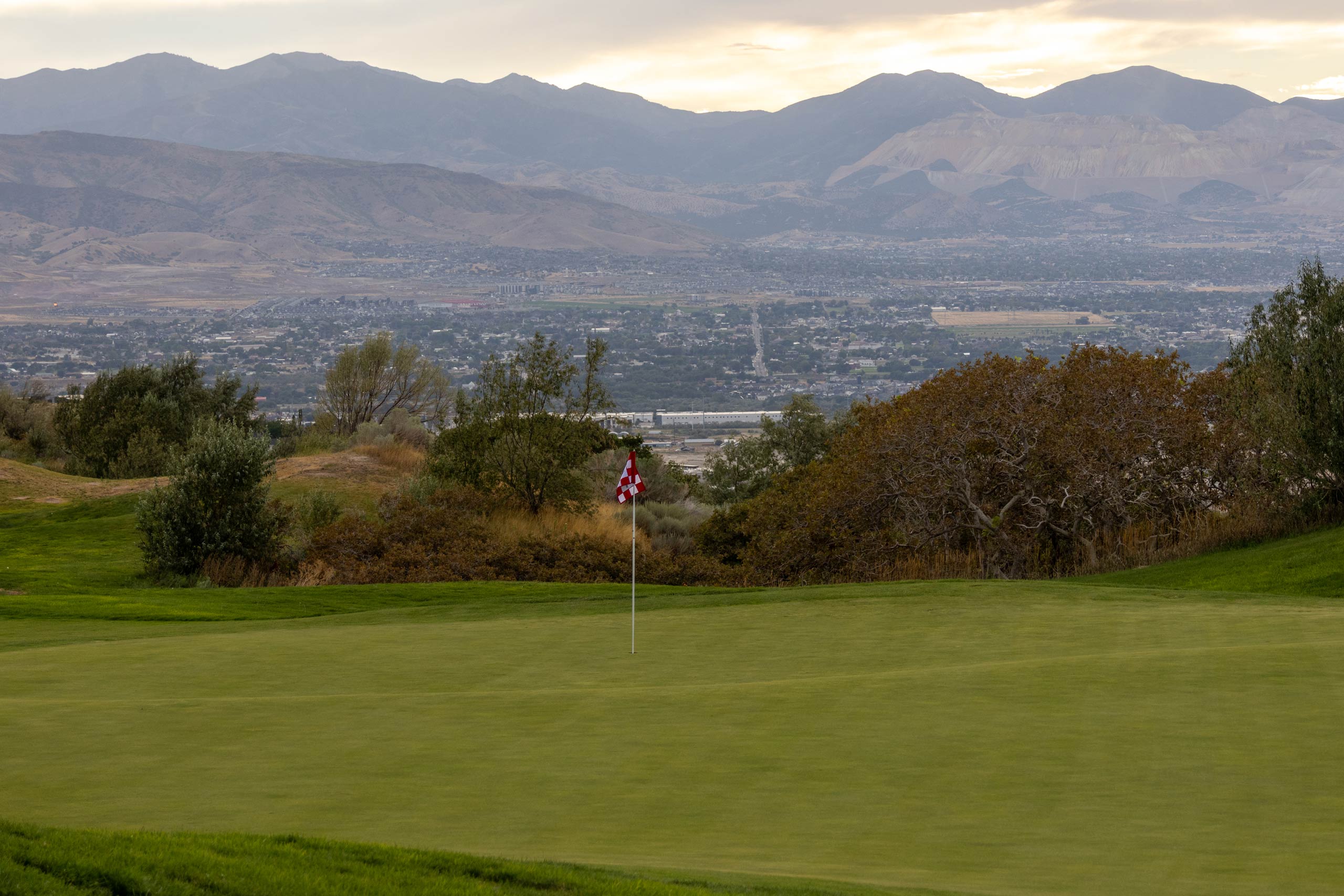The green of a hole on South Mountain golf course in Salt Lake City, with some of the city and mountains in the distance.