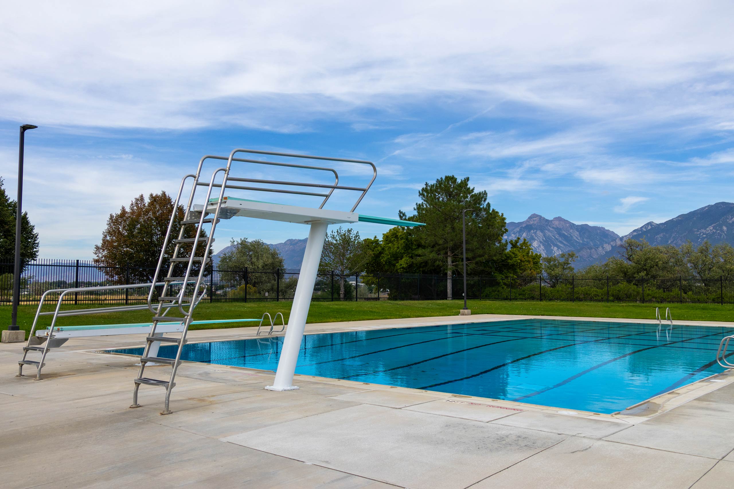 Diving boards and lap lanes at South County Outdoor Pool in Riverton, Utah, with trees and mountains in the distance.